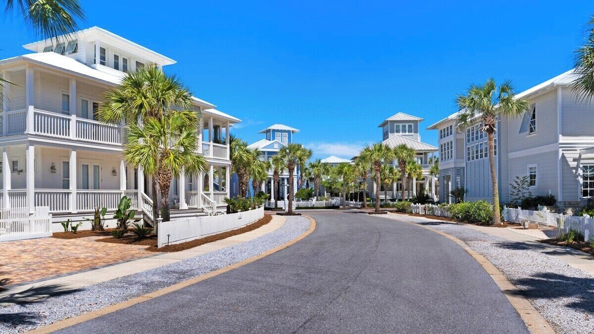 A coastal street lined with white buildings, palm trees, and a clear blue sky.