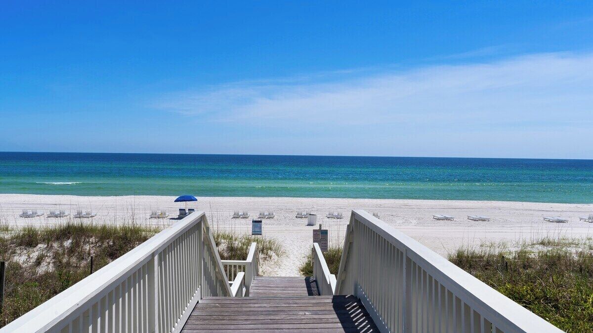 A wooden boardwalk leading to a beach with white sand and clear blue water.