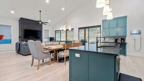 Una cocina moderna con una isla central, un comedor con mesa y sillas de madera, y una sala de estar con sofá y televisor.