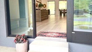Un interior moderno con entrada de puerta de cristal, felpudo de bienvenida, planta en maceta y lámpara colgante.