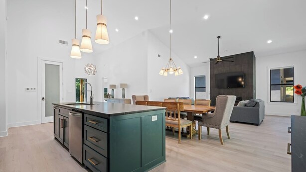 Cocina moderna con isla central, zona de comedor con mesa y sillas de madera, y espacio de sala de estar con sofá y televisor.