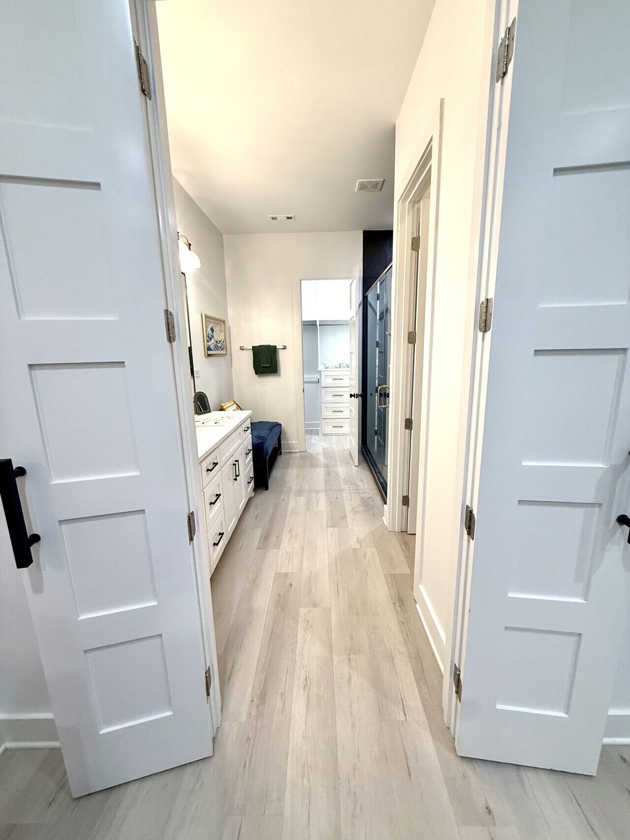Um corredor com portas brancas, uma cômoda, um banco e um armário com gavetas.