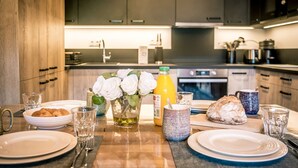 A modern kitchen with dark cabinets, a wooden countertop, and various breakfast items including bread, a bottle of orange juice, and a vase with white flowers.