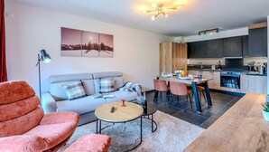 A modern living room with a sofa, a round coffee table, and a dining area with chairs and a table.