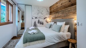 A bedroom with a bed, a wooden wall, a mountain mural, and a window.