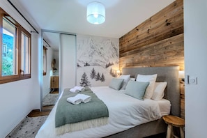 A bedroom with a large bed, a wooden headboard, a mountain mural, and a window with a view. - Charming Apartment – Ideal for skiing and MTB (MORZINE)