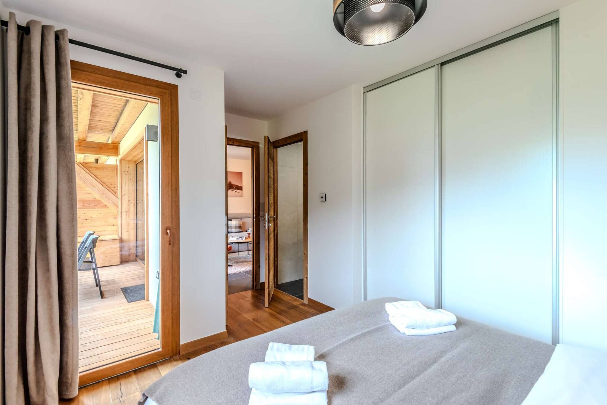 Ein Schlafzimmer mit einem Bett, Holzboden, einer Schiebetür und Blick auf einen Balkon.