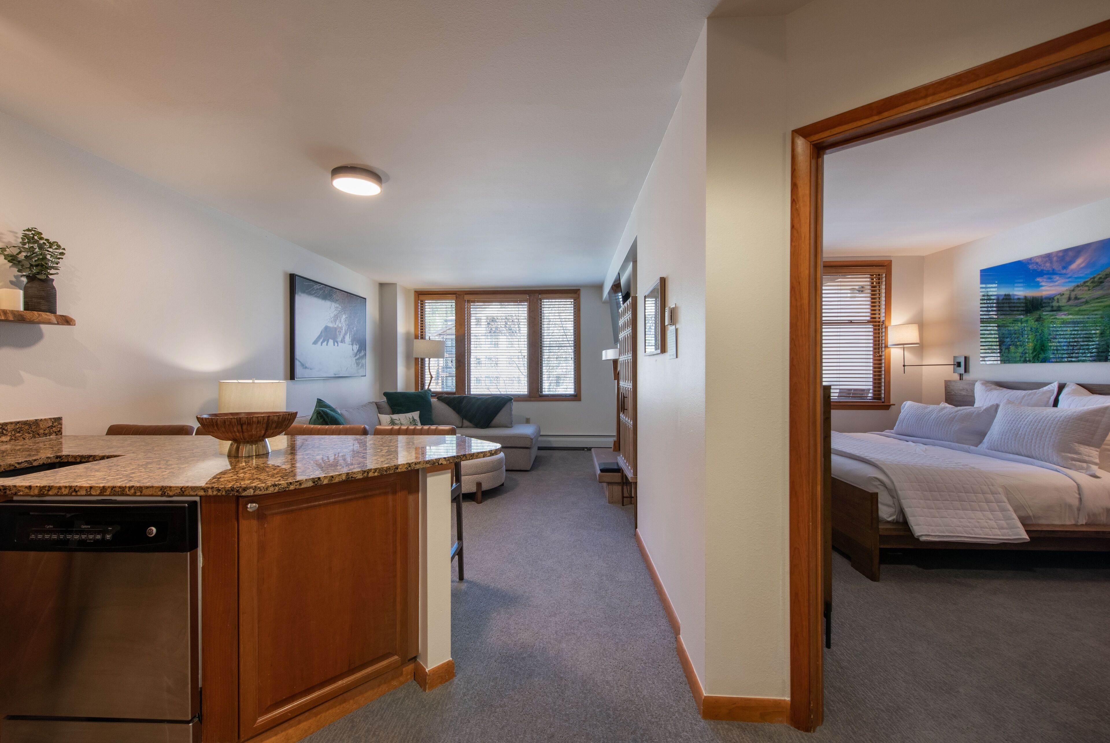 A modern kitchen with a built-in dishwasher, a dining area with a round table and chairs, a cozy living room with a sofa and a coffee table, and a bedroom with a bed and a nightstand.