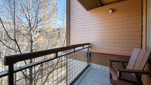 A balcony with a wooden railing, a chair, and a view of trees.