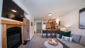A modern living room with a fireplace, a grey sofa, a wooden coffee table, and a kitchen in the background.