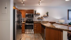 A modern kitchen with stainless steel appliances, wooden cabinets, granite countertops, and a built-in island.