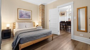 Une chambre avec un lit, des tables de chevet, un ventilateur de plafond, un mur en briques et un coin repas avec des chaises et une table.