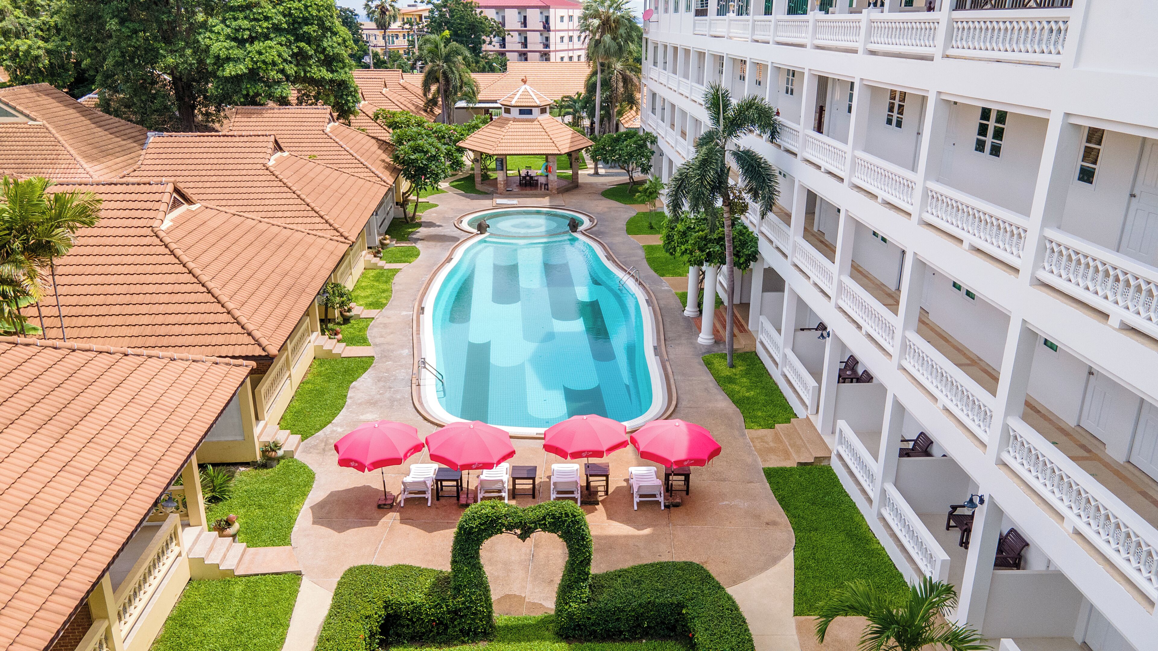 A hotel with a swimming pool, outdoor seating, and a heart-shaped hedge.