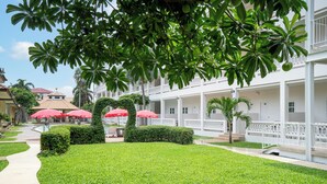Un cortile di hotel con un prato curato, ombrelloni rossi e un edificio bianco con balconi.