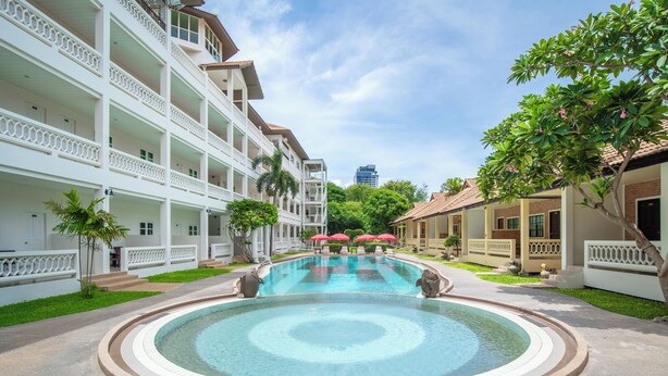 Un hotel con piscina centrale, numerosi balconi e vegetazione rigogliosa.