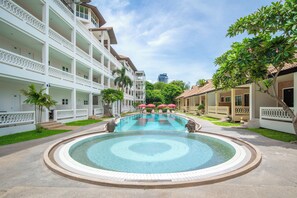 Un hotel con piscina central, varios balcones y abundante vegetación.