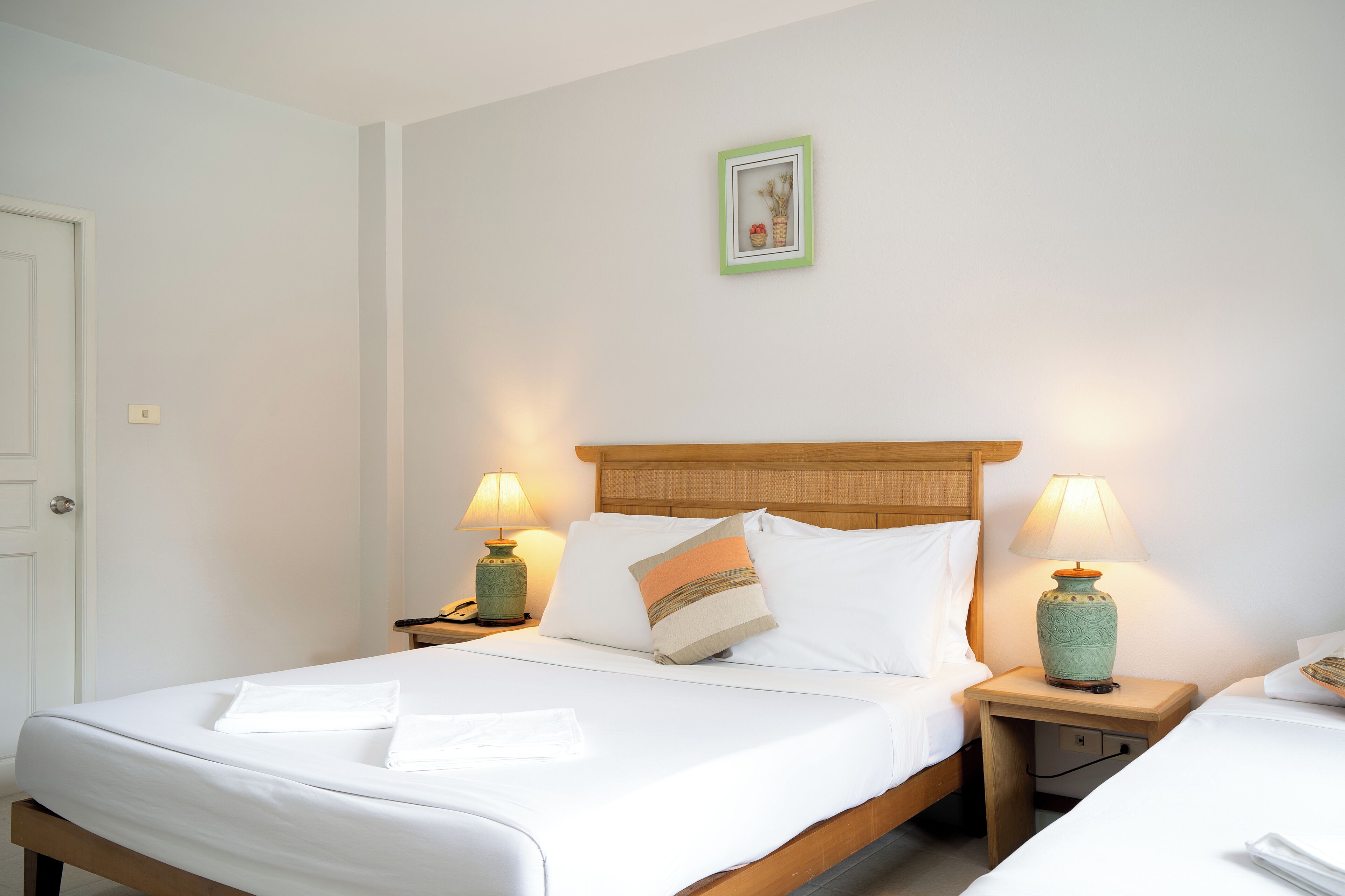 A hotel room with a bed, two bedside tables with lamps, a nightstand, and a framed picture on the wall.