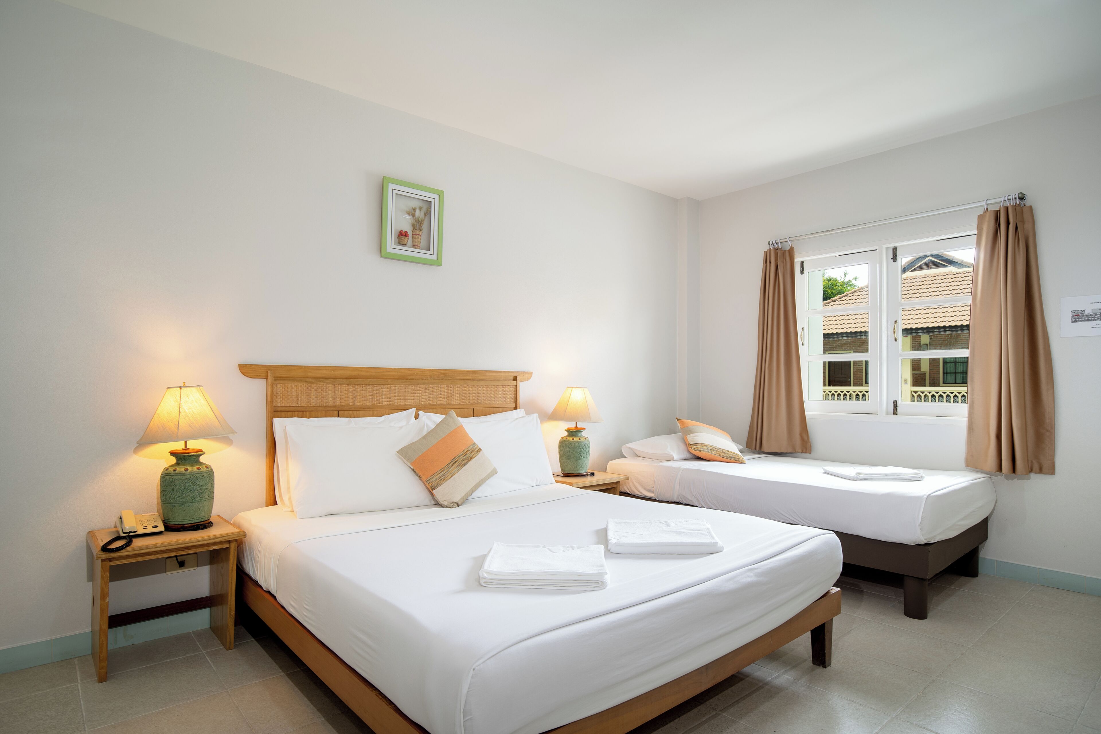 A hotel room with two beds, a nightstand with a lamp, a window with curtains, and a framed picture on the wall.