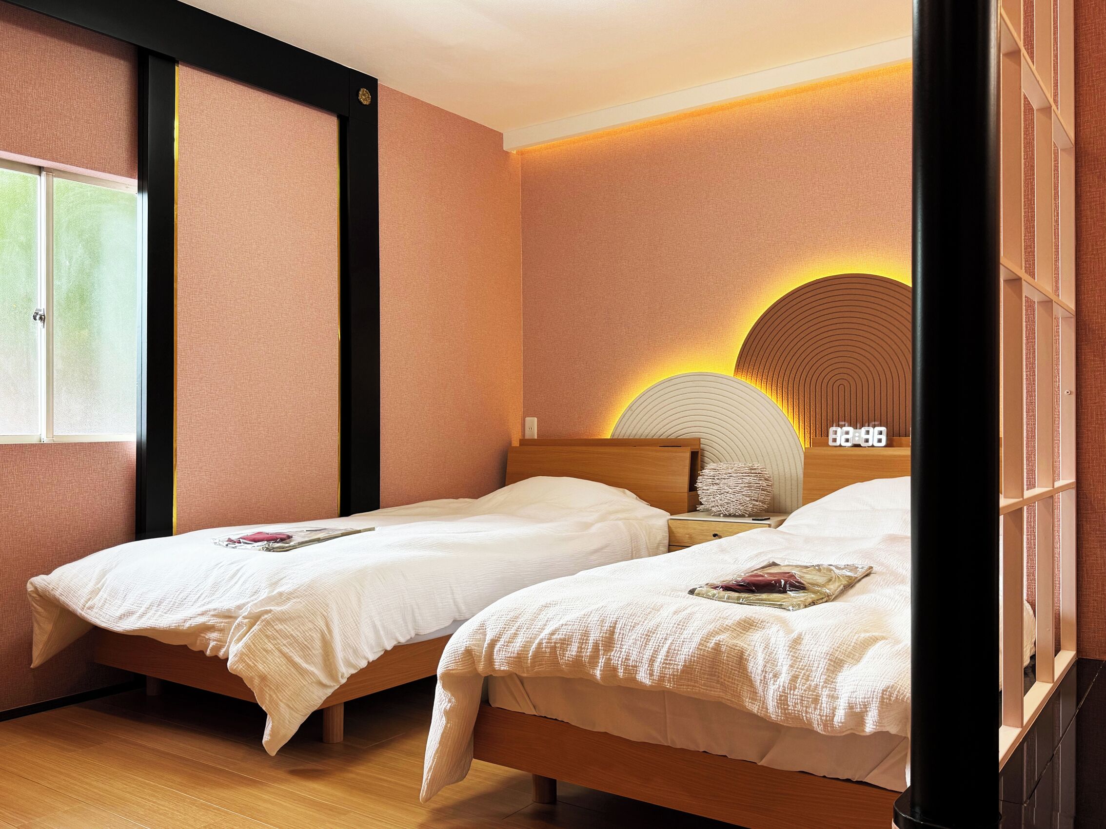 Ein Hotelzimmer mit zwei Einzelbetten, einem Holzkopfteil, einer Wanduhr und einem Fenster.
