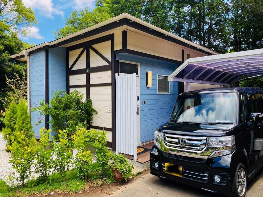 A small blue house with a garage, a black SUV parked in front, and a solar panel on the roof.