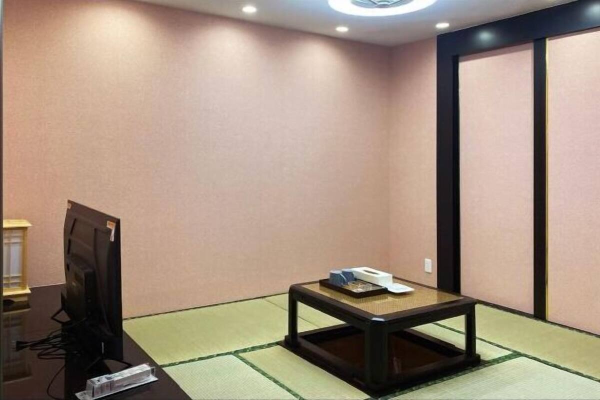 A room with a tatami mat floor, a low table with a telephone, and a television on a stand.
