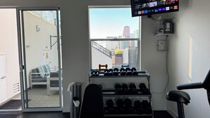 Ein Fitnessraum mit Kurzhanteln, Laufband und Fernseher, der Streamingdienste anzeigt.