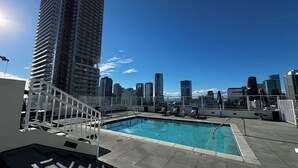 Ein Pool auf dem Dach mit Blick auf die Stadt, einer Glasrelung und einigen Liegestühlen.