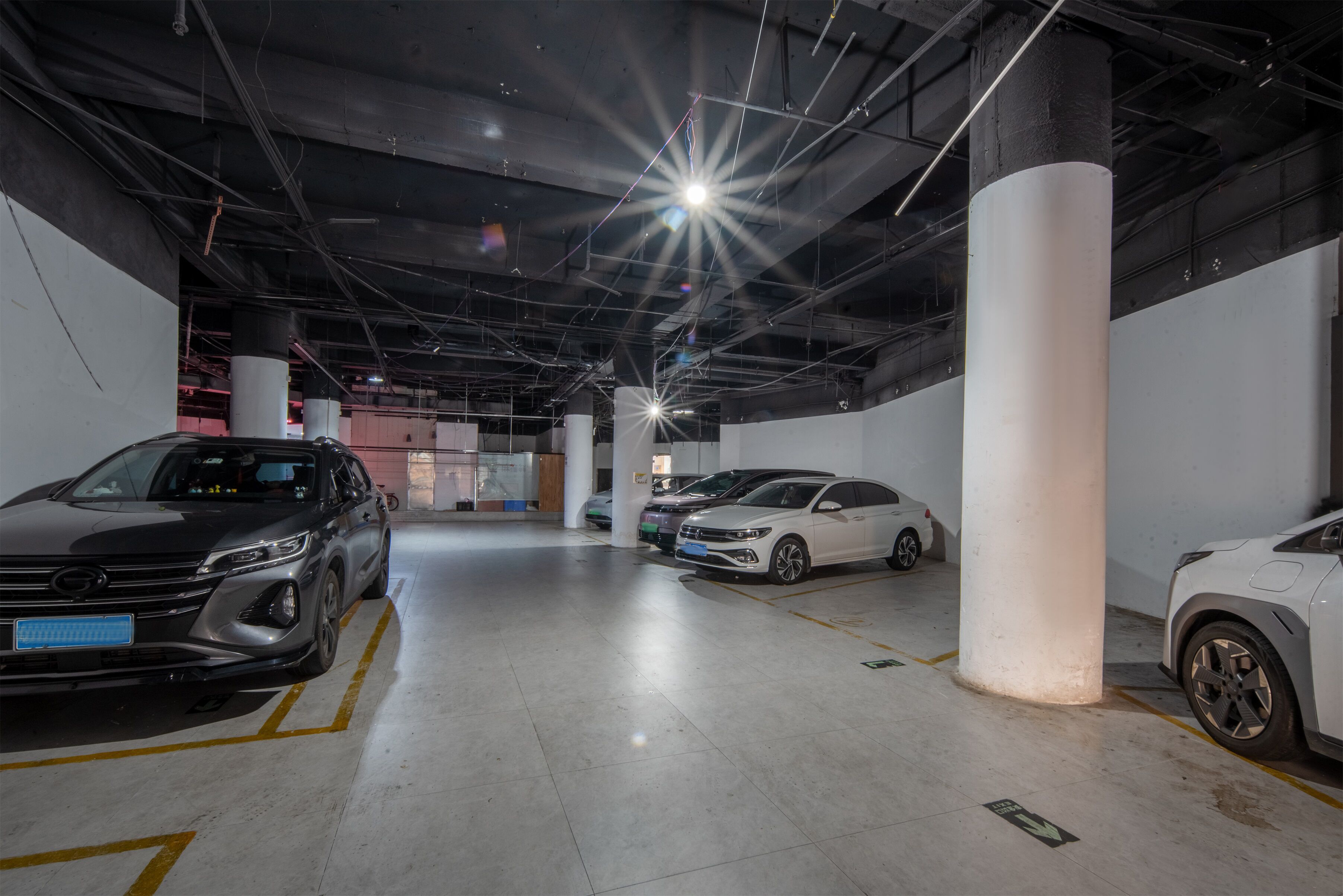 Un garaje para estacionamiento con varios automóviles, pilares de hormigón e iluminación superior.