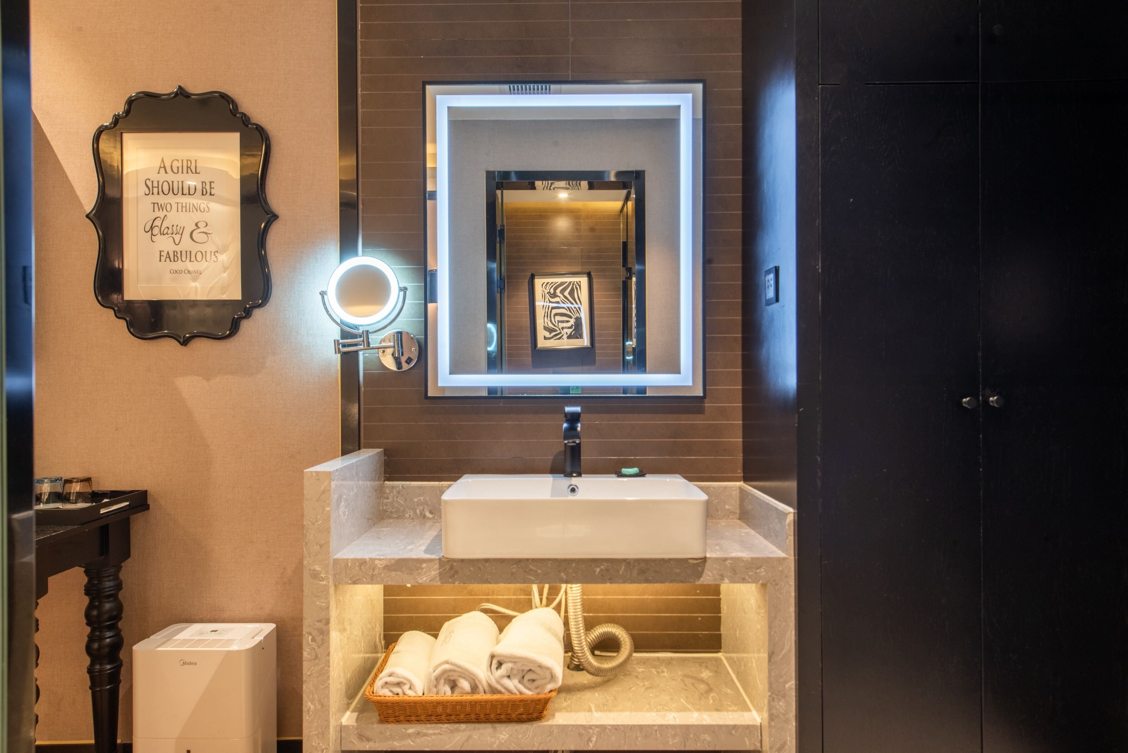 A bathroom with a vanity, a mirror, a framed quote, a towel rack, and a wall-mounted light.