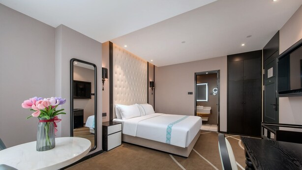 A hotel room with a bed, a desk, a chair, a mirror, a TV, and a vase with flowers. - Pazhou XANA Deluxe International Hotel Pazhou Convention and Exhibition Center Changgang Subway Metro Branch - Free Shuttle Bus to Canton Fair Complex During Canton Fair Period (Guangzhou)