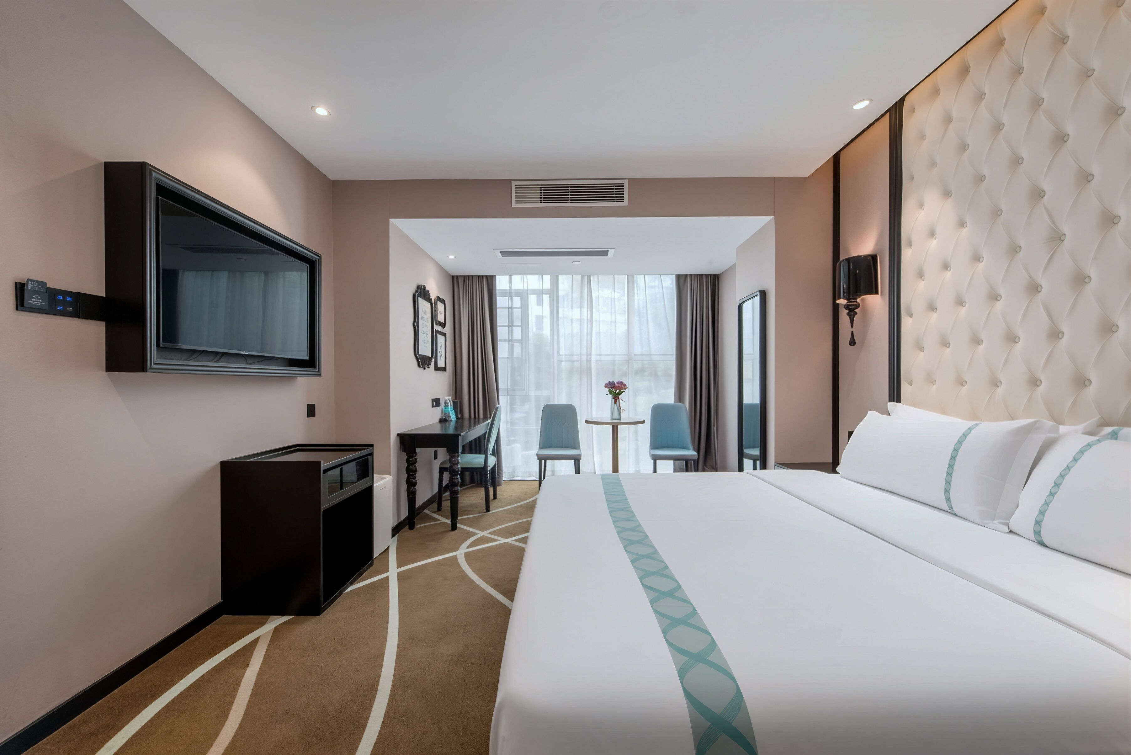 A hotel room with a bed, a desk, a TV, and a view of the outside.