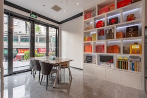 A modern interior with a dining table, chairs, a bookshelf, and a view through the glass door. - Pazhou XANA Deluxe International Hotel Pazhou Convention and Exhibition Center Changgang Subway Metro Branch - Free Shuttle Bus to Canton Fair Complex During Canton Fair Period (Guangzhou)