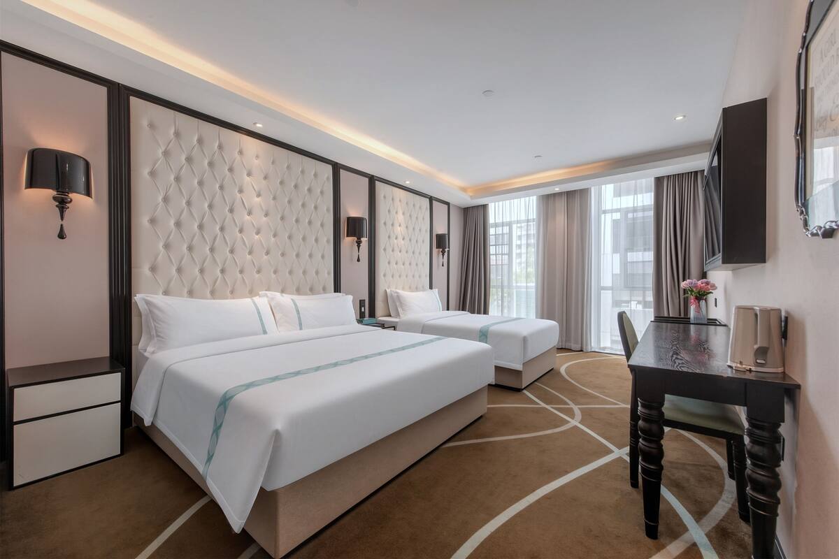 A hotel room with two beds, a desk, a TV, and a large window.