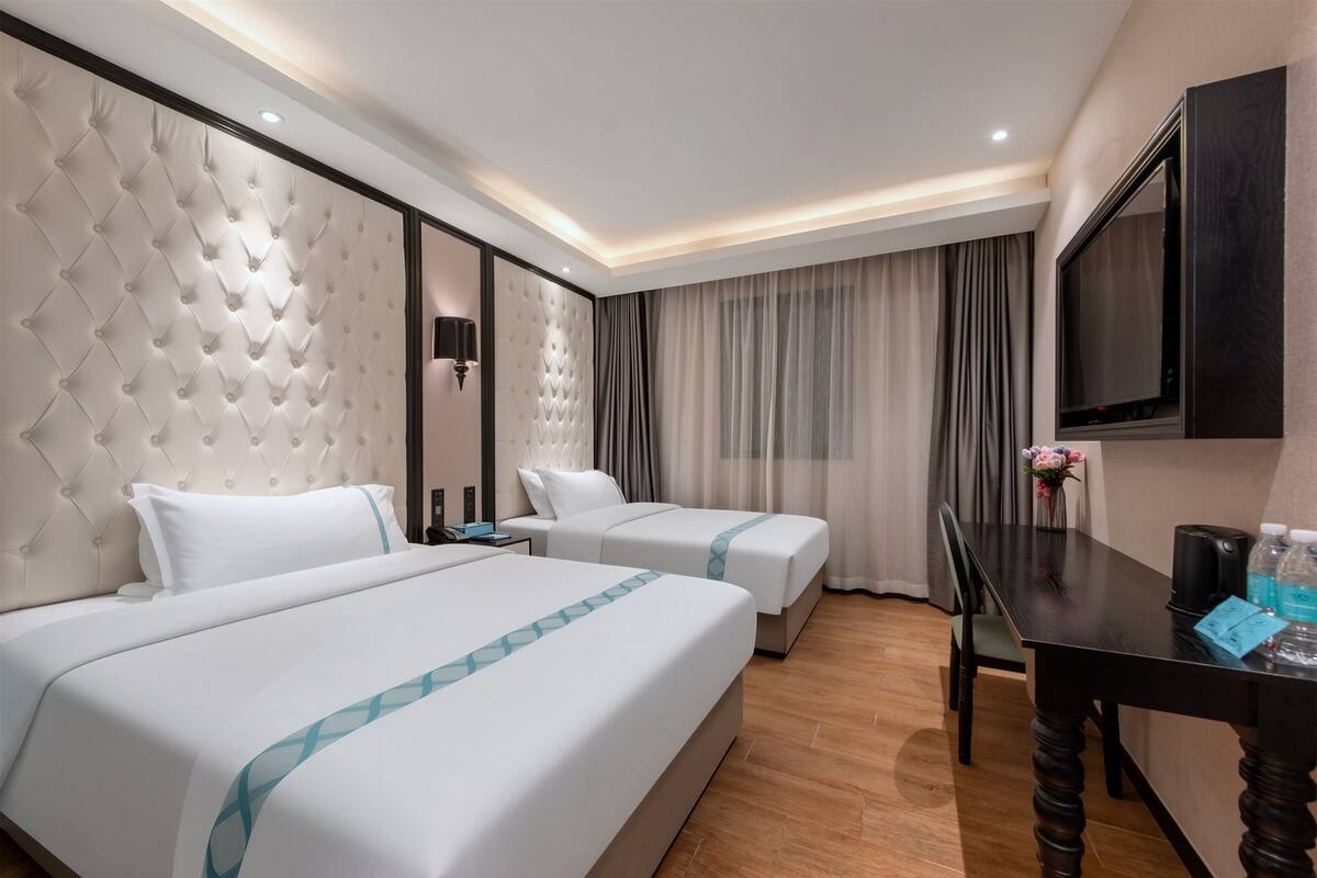 A hotel room with two beds, a desk, a TV, and a wall-mounted TV.