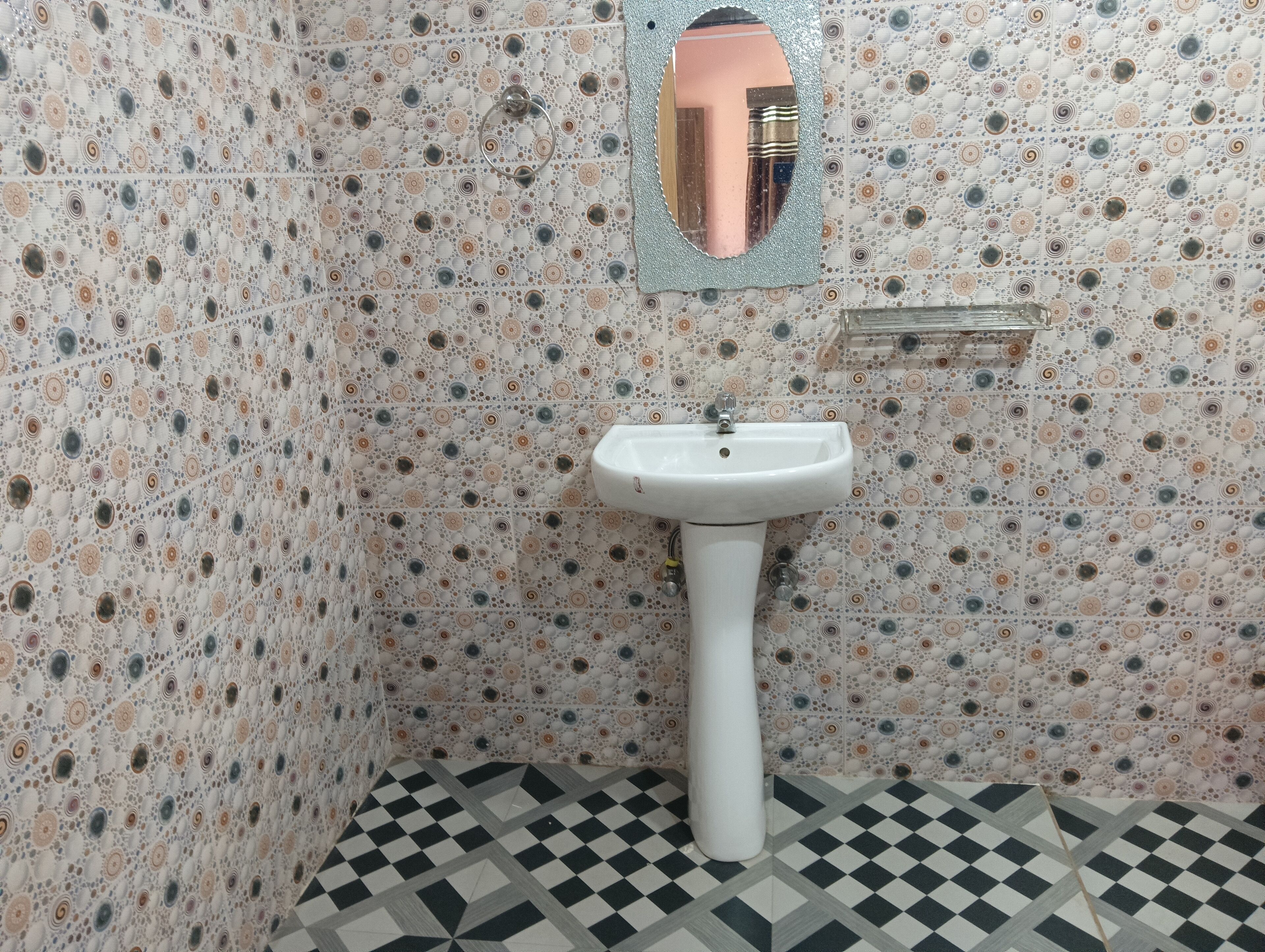 Un baño con pared de azulejos estampados, un lavamanos blanco y un espejo.