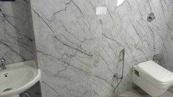 Baño con lavamanos, inodoro y zona de ducha blancos, todo con suelo y paredes de apariencia marmolada.