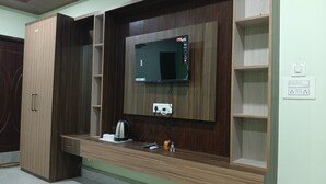 A room with a built-in TV, wooden shelving, and a small table with a kettle and remote controls. - RESORT RUPKATHA (Mal)
