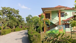 A pathway leading to a building with a green facade and a red roof, surrounded by lush greenery and a mural of a deer. - RESORT RUPKATHA (Mal)