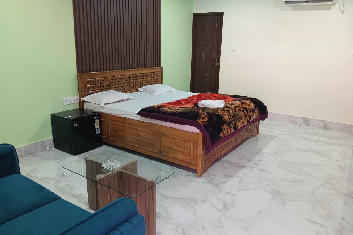 A bedroom with a wooden bed, a glass coffee table, a blue sofa, and a small black cabinet.