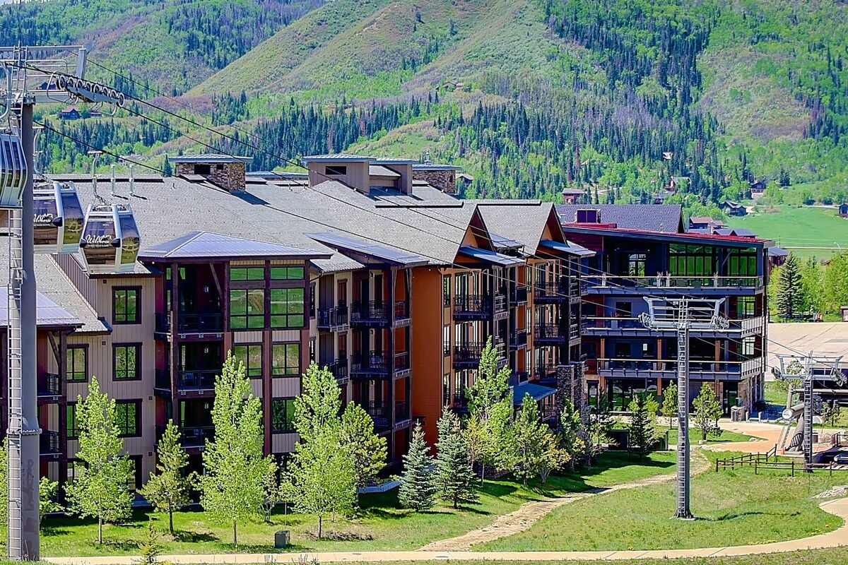 A multi-story hotel with balconies, a ski lift, and a mountainous backdrop.