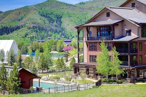 A multi-story building with balconies, a pool, and a mountainous backdrop.