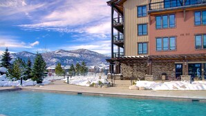 Un espace piscine avec vue sur les montagnes, un bâtiment en pierre et un immeuble à plusieurs étages doté de balcons.