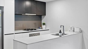 Een moderne keuken met witte kasten, een zwart aanrecht, een fornuis, een spoelbak en een koffiezetapparaat.