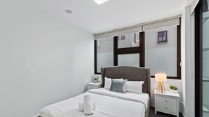 Een moderne hotelkamer met een groot bed, een nachtkastje met lamp en een raam met jaloezieën.