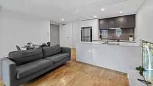 Een moderne keuken met witte kastjes en roestvrijstalen apparatuur, een grijze bank en een eethoek met een tafel en stoelen.