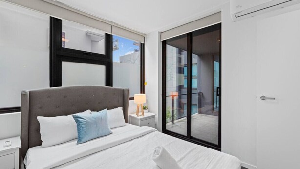 Een hotelkamer met een groot bed, een nachtkastje, een lamp en een glazen schuifdeur naar een balkon.
