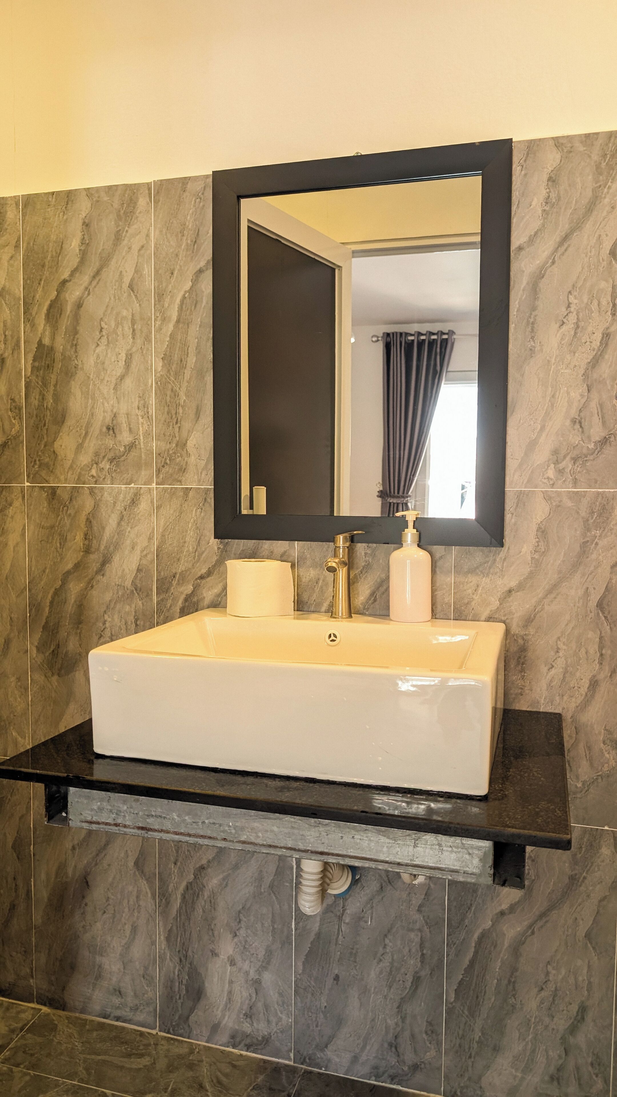 A bathroom with a white sink, black countertop, and marble tiles.