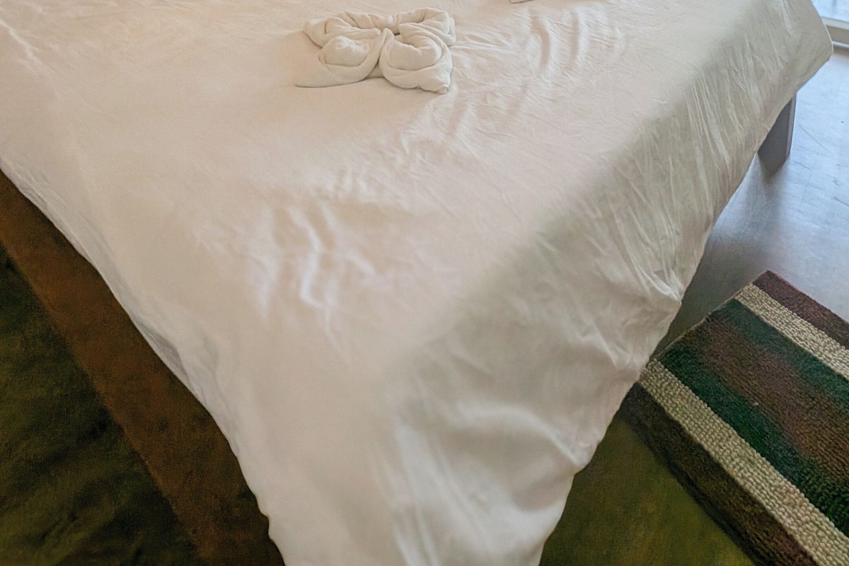 A hotel room with a large bed, two pendant lights, a window with curtains, and a view of the outside.