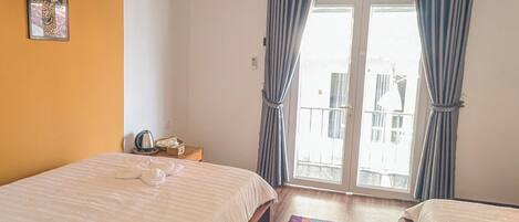 Una habitación con dos camas, una lámpara en el techo, una ventana con cortinas y una puerta que da a un balcón exterior.