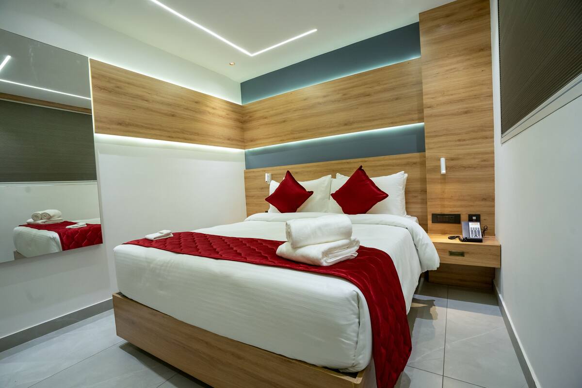A modern hotel room with a large bed, wooden headboard, and a bedside table with a phone and a lamp.